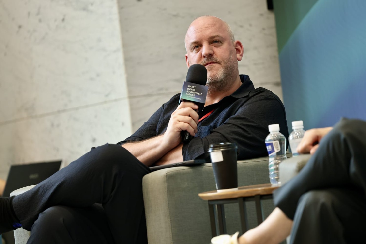 Adrian Watkins on a sofa with a microphone during the Smart Living, Sustainable Future 2025 fireside in Taipei.