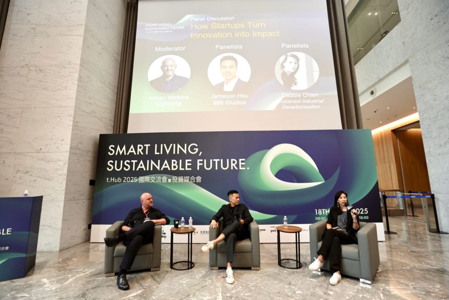 Adrian Watkins moderating the startup panel at Smart Living, Sustainable Future 2025 in Taipei. Three seated speakers.